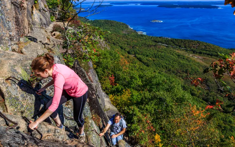 Two hikers ascend a sheer cliff trail by way of historic iron rung ladders.
