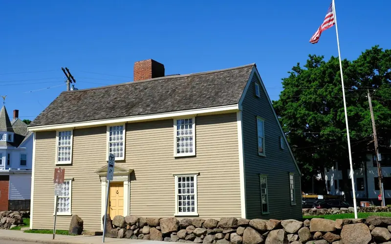 A New England "salt-box" style house with light gray siding and a beige door.