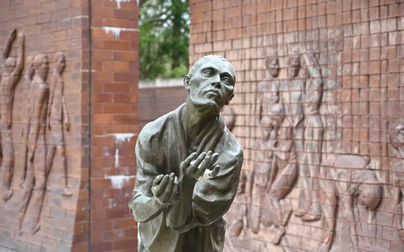 stone statue stands with his arms stretched forward. Two large stone walls sit behind him.