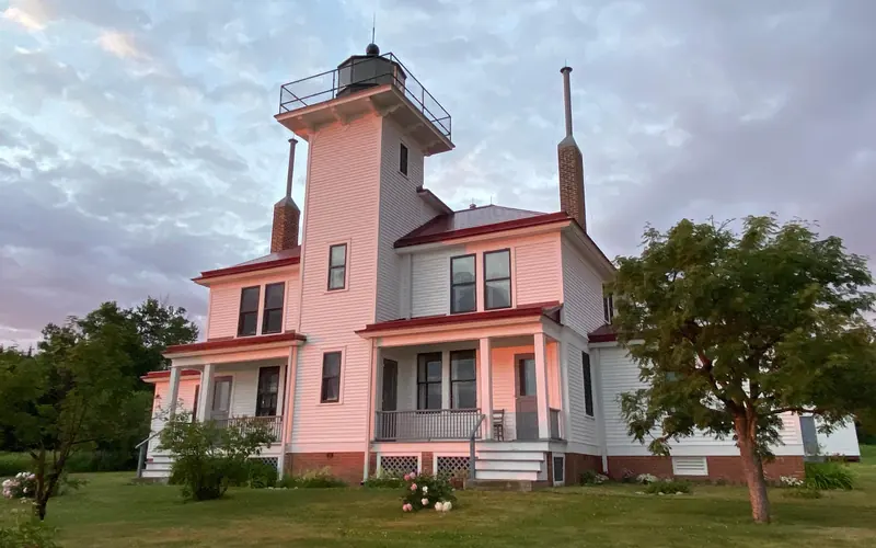 A two story white house with a light tower in the middle, reflects the colors of the setting sun.