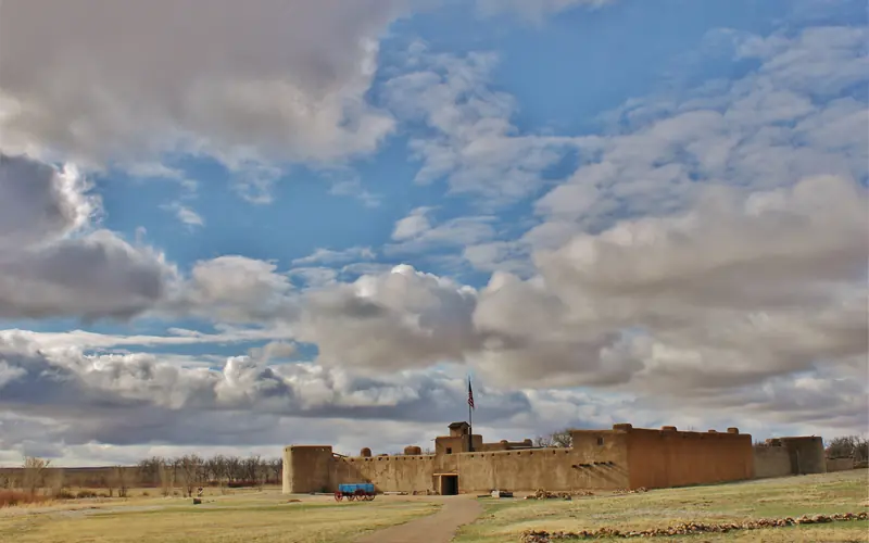 Bent's Old Fort with shortgrass prairie in foreground and blue sky and clouds above