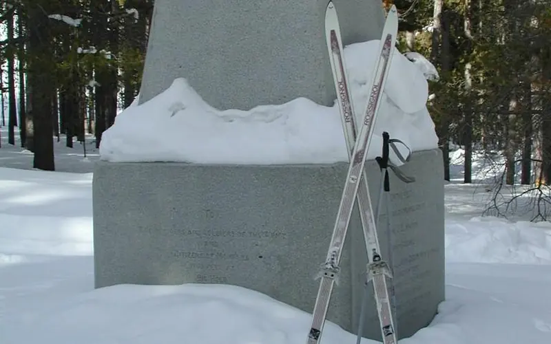 cross country skis rest against a large granite monument on a snowy day.