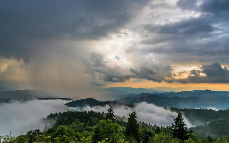 Storm clouds breaking over the mountains at sunset, with fog hugging the valleys