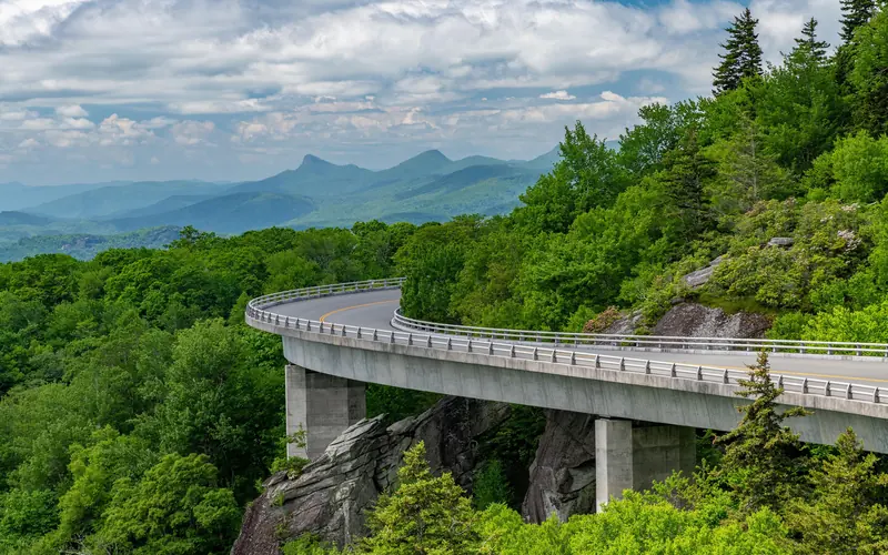 A roadway on piers follows the curve of a mountainside, running toward distant mountains.