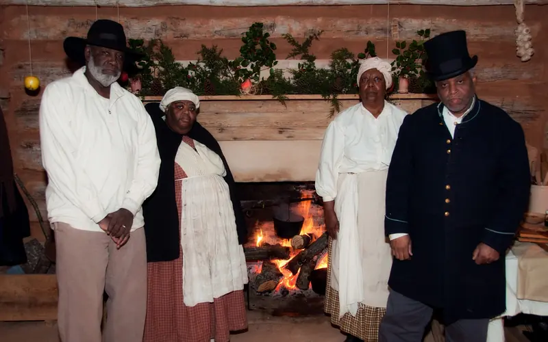 Four people dressed as enslaved people in front of the fireplace in cabin