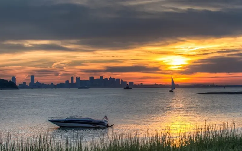 An image of the sun setting over the Boston skyline from the Islands