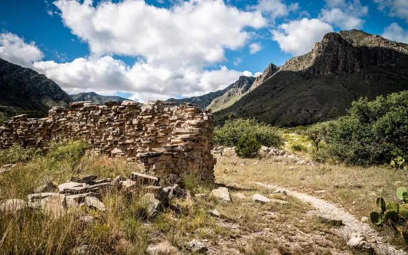 A historic stone wall stands in ruins next to a hiking trail leading into the Guadalupe Mountains NP