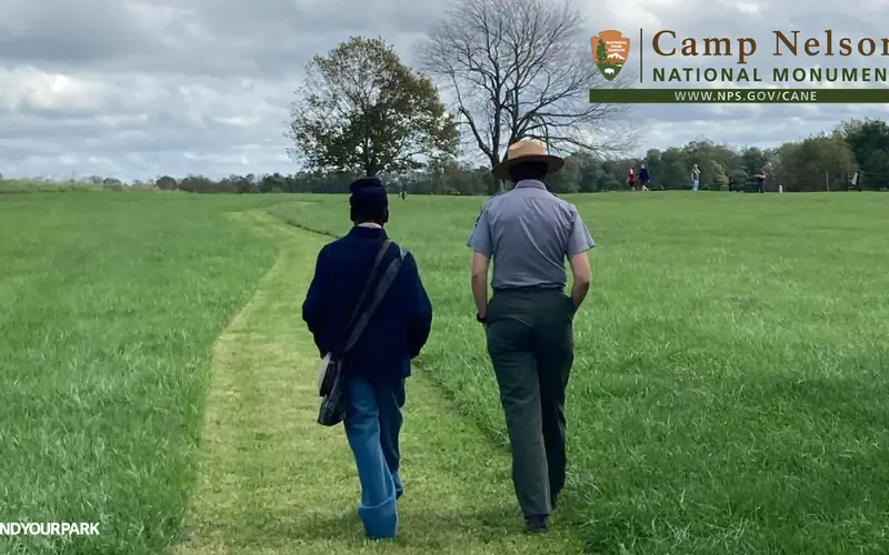 A living historian wearing a US Army Civil War uniform and park ranger walk on a mowed path.