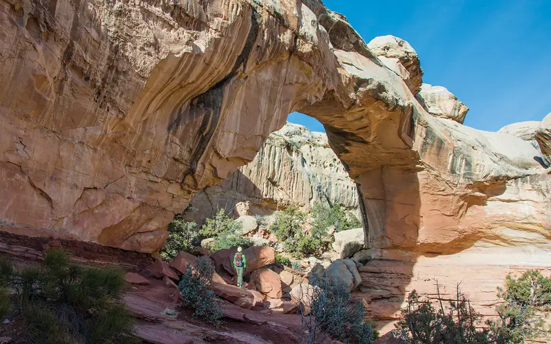 A hiker stands beside Hickman Bridge, a natural sandstone bridge