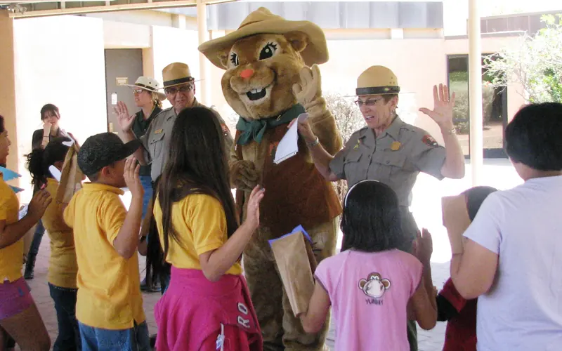 a group of children with hand raised in front of park rangers and ground squirrel mascot