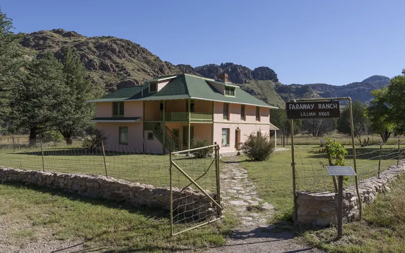 A ranch house in a green field surrounds by low mountains