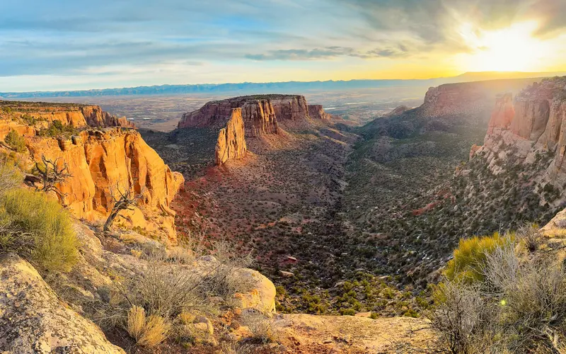 red-orange cliffs frame rolling green canyon bottoms at sunrise