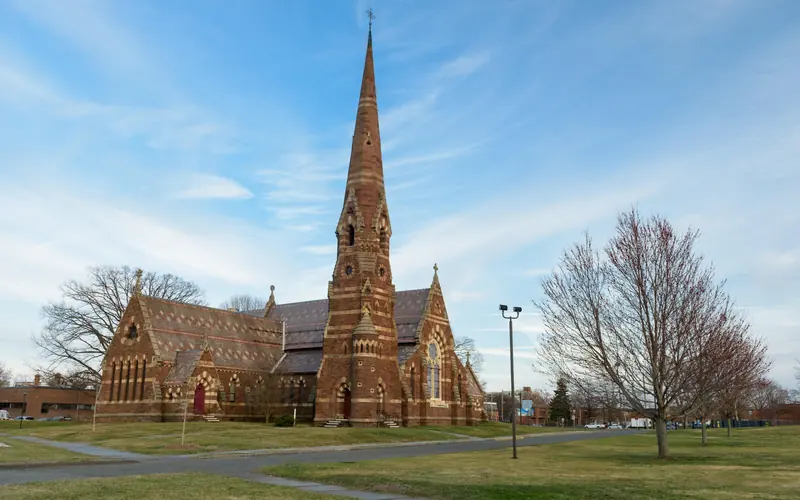 A church and trees against the backdrop of a bight blue sky and clouds.