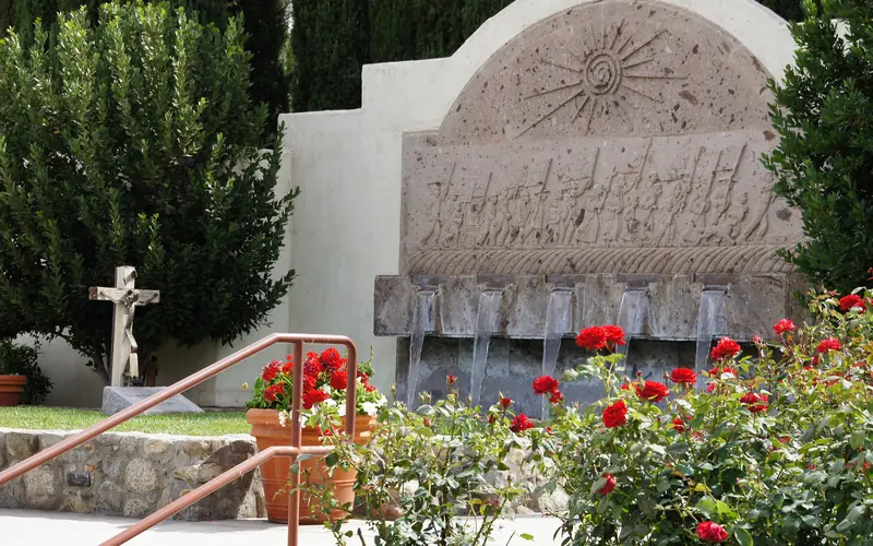 Red roses bloom near a fountain and grave marker