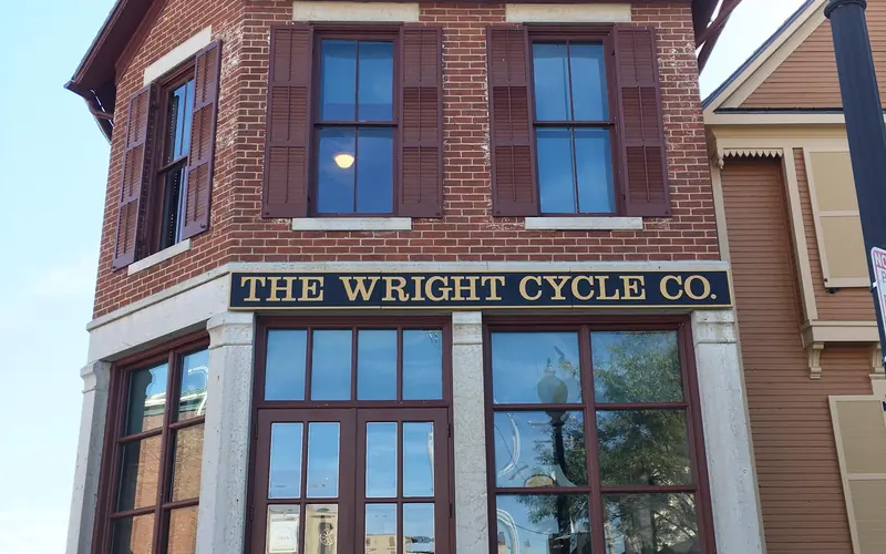 A two-story brick building with tall windows and shutters on them with sign "The Wright Cycle Co."