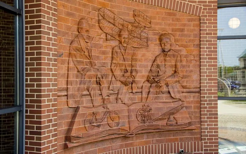 A brick wall with artwork of three men and an airplane etched out of the brick.