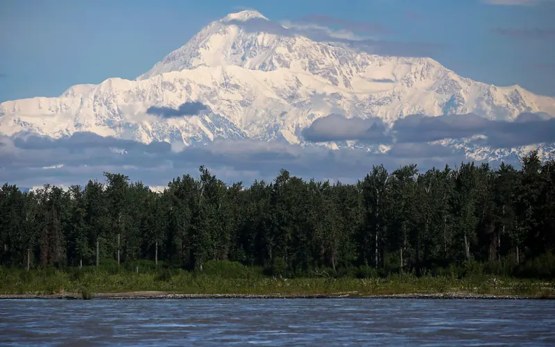 A huge snowy mountain looming over a landscape of forests and water