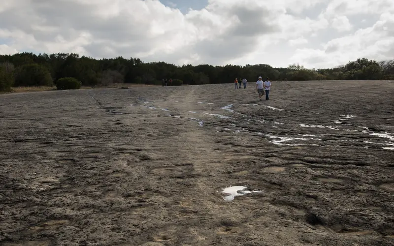rock indentations in a dry creek with five people walking under clouds