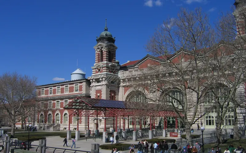 Brick and limestone building with maroon canopy leading to entrance.