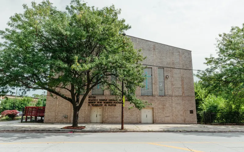 A multi-story tan brick church along a road. A tree stands in front.