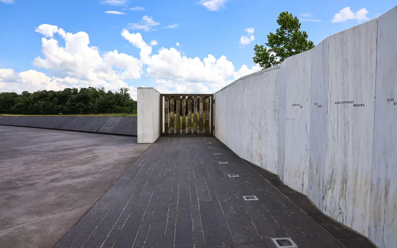 A white marble wall with names engraved on the the walls and the Ceremonial Gate. Blue sky above.