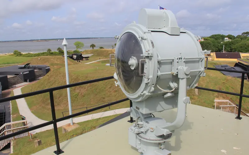 Center of image is round metal and glass signal light with grassy hills hills in background