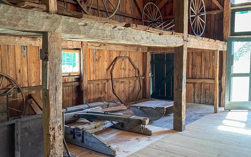 The sun shines upon wooden wagon wheels and other antique farm implements lining the rustic hewn wal