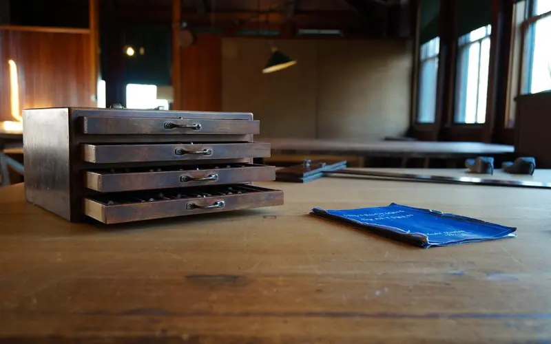 Dark wood box with four shallow drawers on large wooden table with blueprint