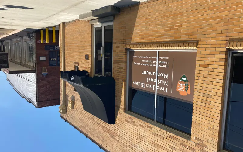 street view of a yellow brick bus depot, with a black awning and NPS sign, and an alley entrance.