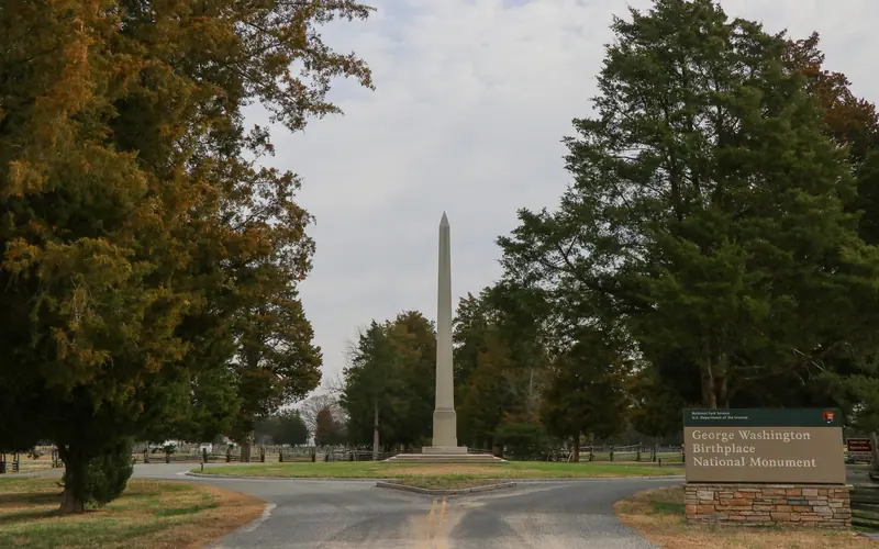 White obelisk in a roundabout, surrounded by trees and the park sign