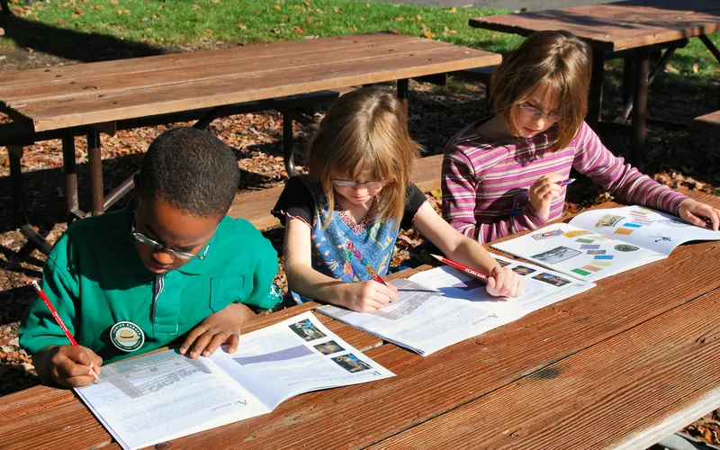 three children seated at a picnic table working on a Glen Echo Park Junior Ranger Booklet.