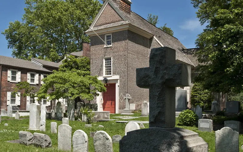 A color photo of the Gloria Dei Church yard showing tombstones with the church in the background.