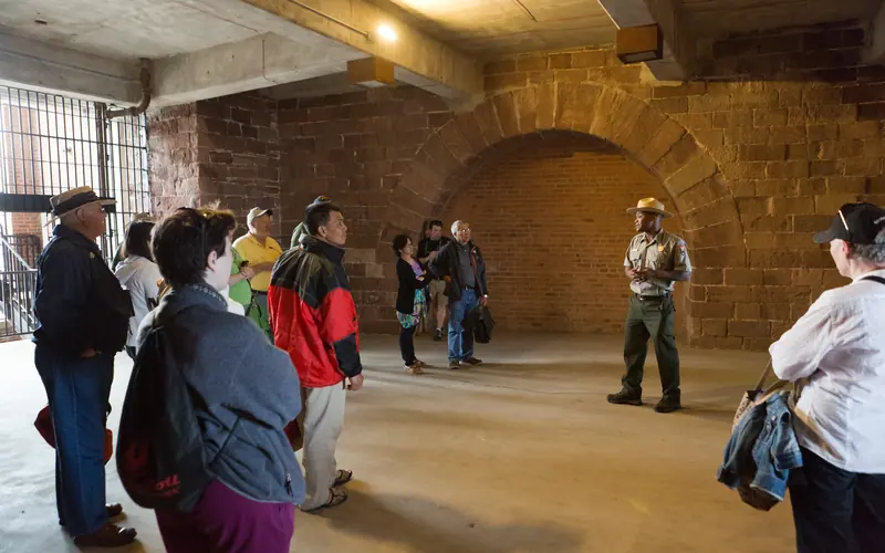 A park ranger talking to a group of visitors inside a large stone room in a fort.