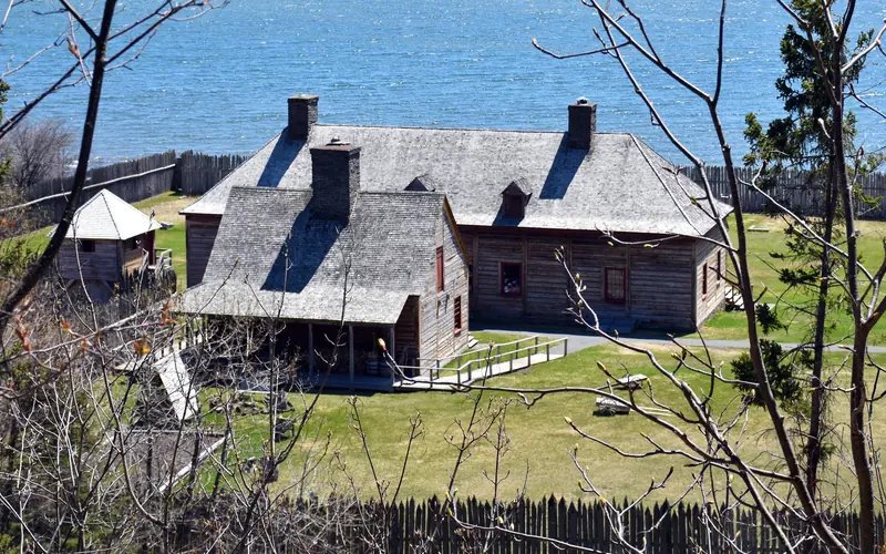 Historic wooden buildings on a bright green lawn in front of a lake.