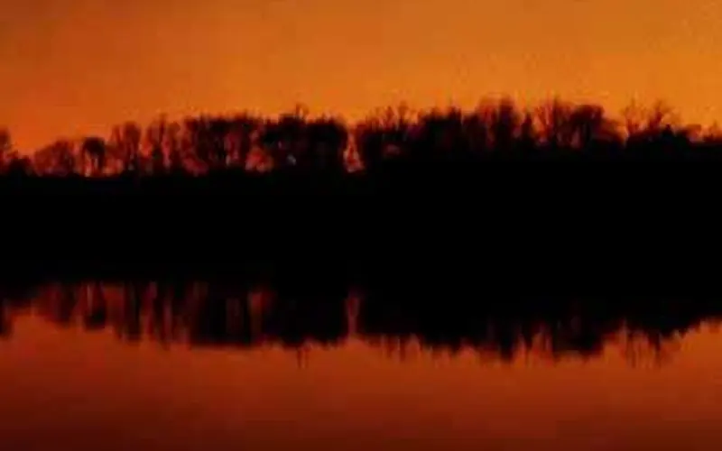 Bright white comet in the early night sky reflects over the river.