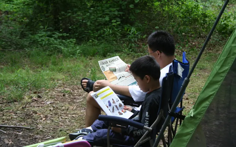 Father and son sitting in chairs reading in the Greenbelt Park campground
