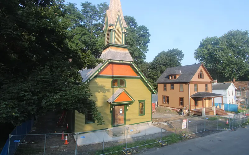 Wooden church with tall steeple, with construction equipment out front.