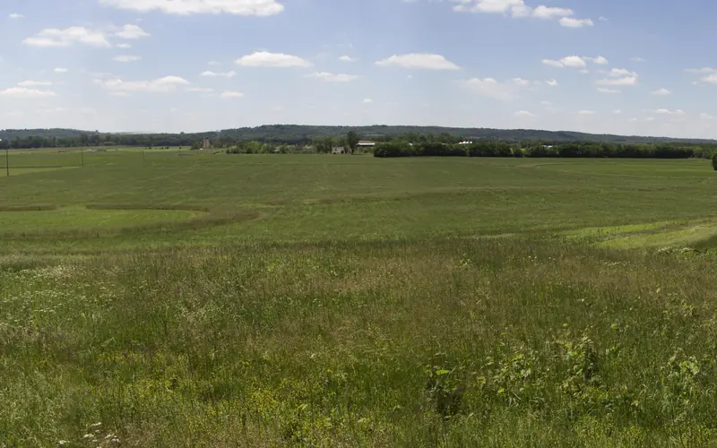 A green, grassy field with taller areas of uncut grass in geometric shapes under a partly cloudy sky
