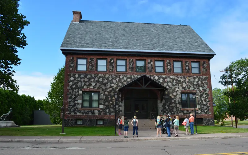 Two story stone and brick building. a ranger leads a group of visitors in front or the steps