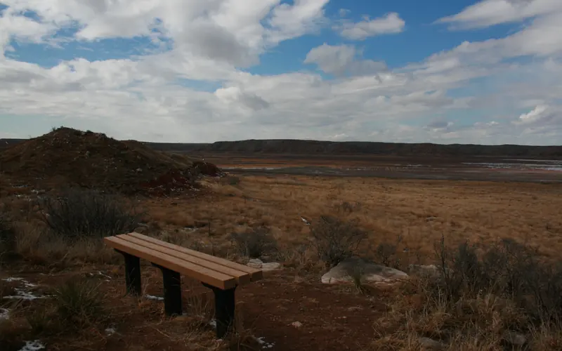 A bench on the Harbor Bay Trail, overlooking Lake Meredith. The sky is blue with white clouds.