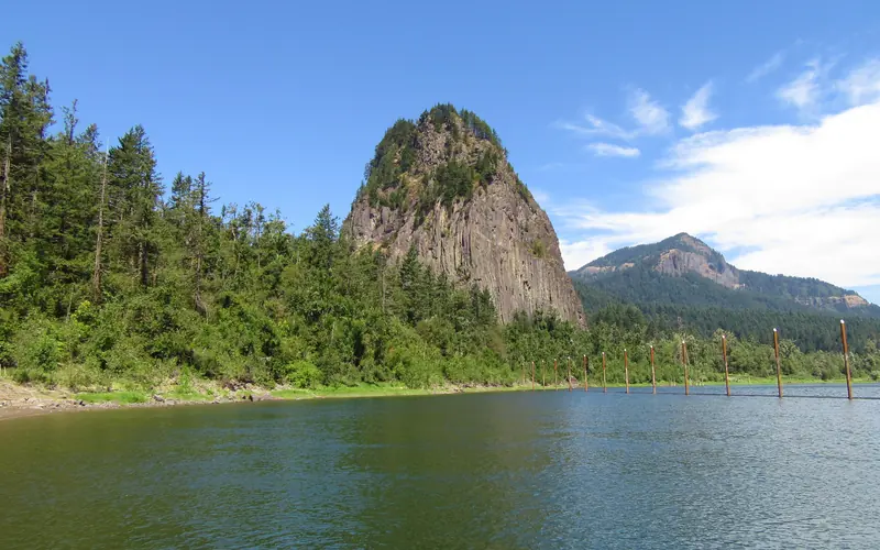 Water in the foreground with large conical rock on shore