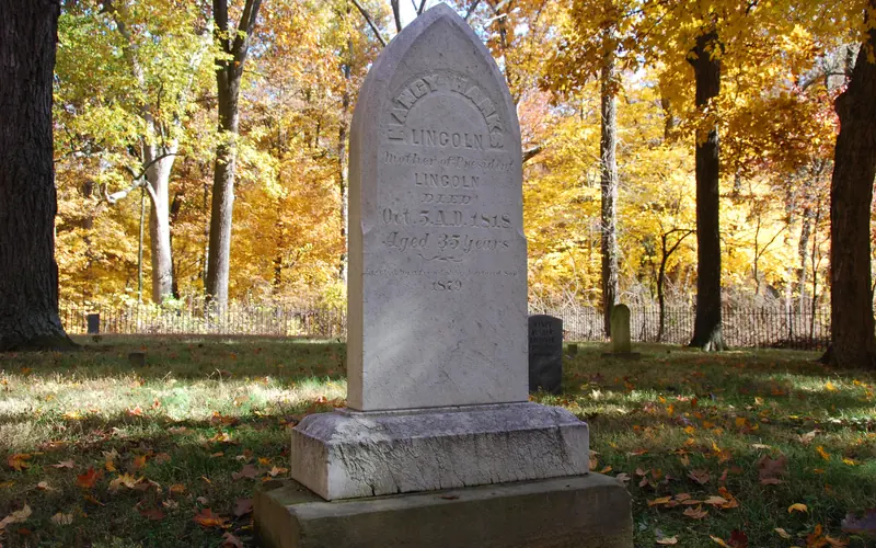 White marble headstone of Nancy Hanks Lincoln in cemetery surrounded by iron fence and trees.