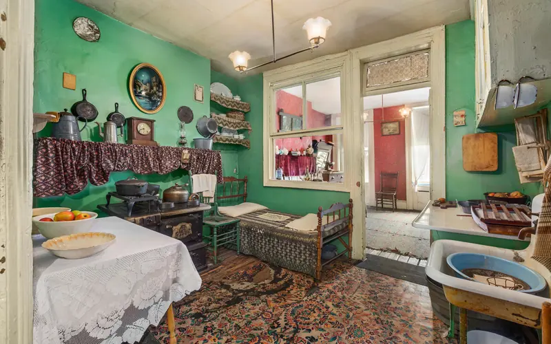 A tenement kitchen with cast iron posts, old stove, and a bed next to the stove