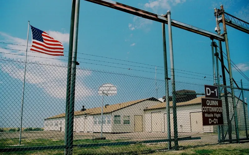 A brown building behind a tall fence with warning signs