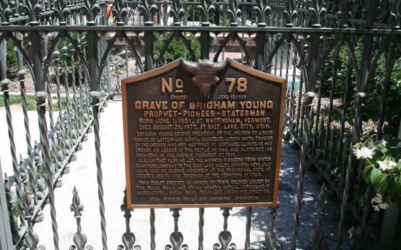 A bronze plaque with description on a metal fence surrounding Brigham Young's grave.