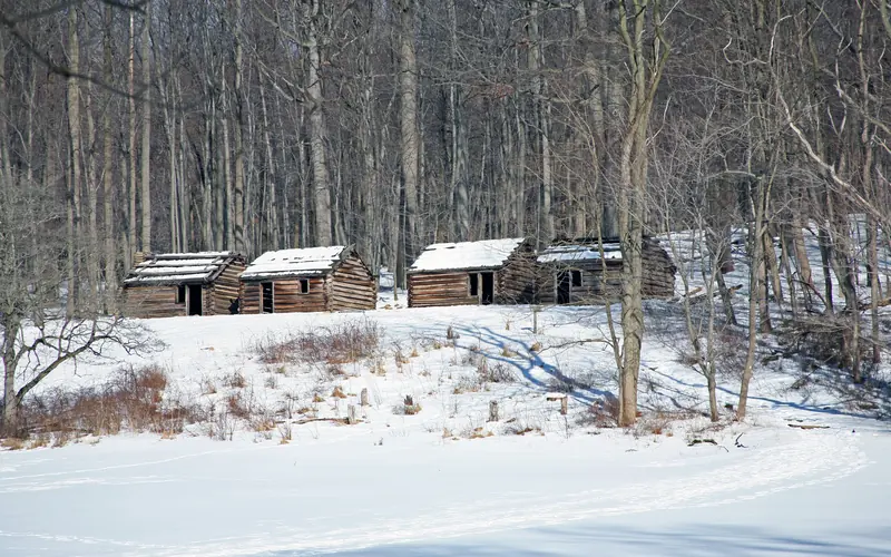 Four replica wooden soldier huts on a hillside in winter