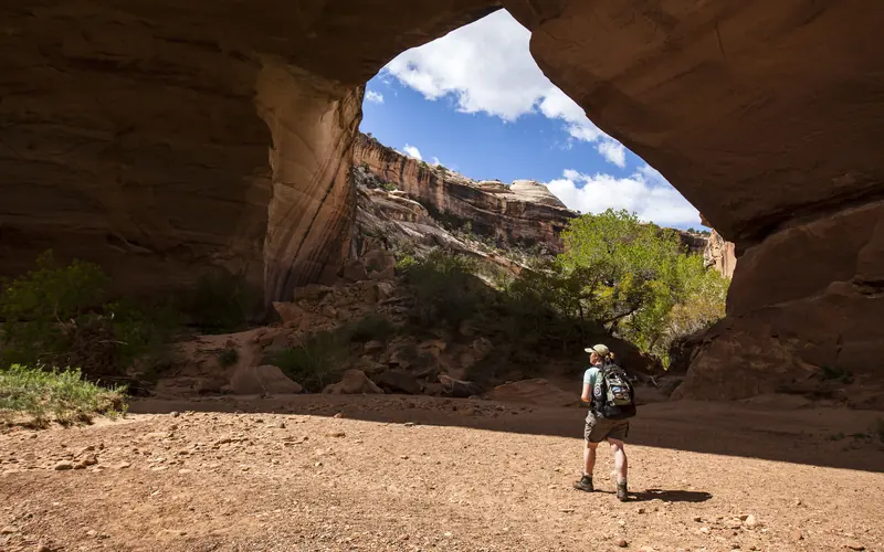 a hiker standing below a massive natural bridge