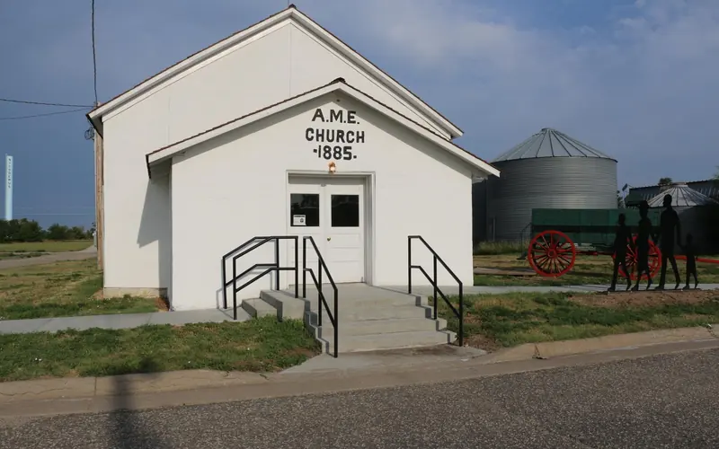 White stucco church with white double doors and text above the doors that reads "A.M.E. CHURCH 1885"