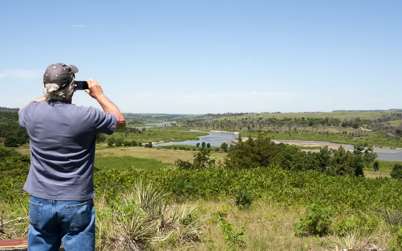 A man takes a photo of a meandering river from an overlook.