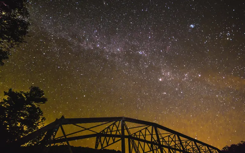 A star-filled night sky above the silhouette of a truss-bridge